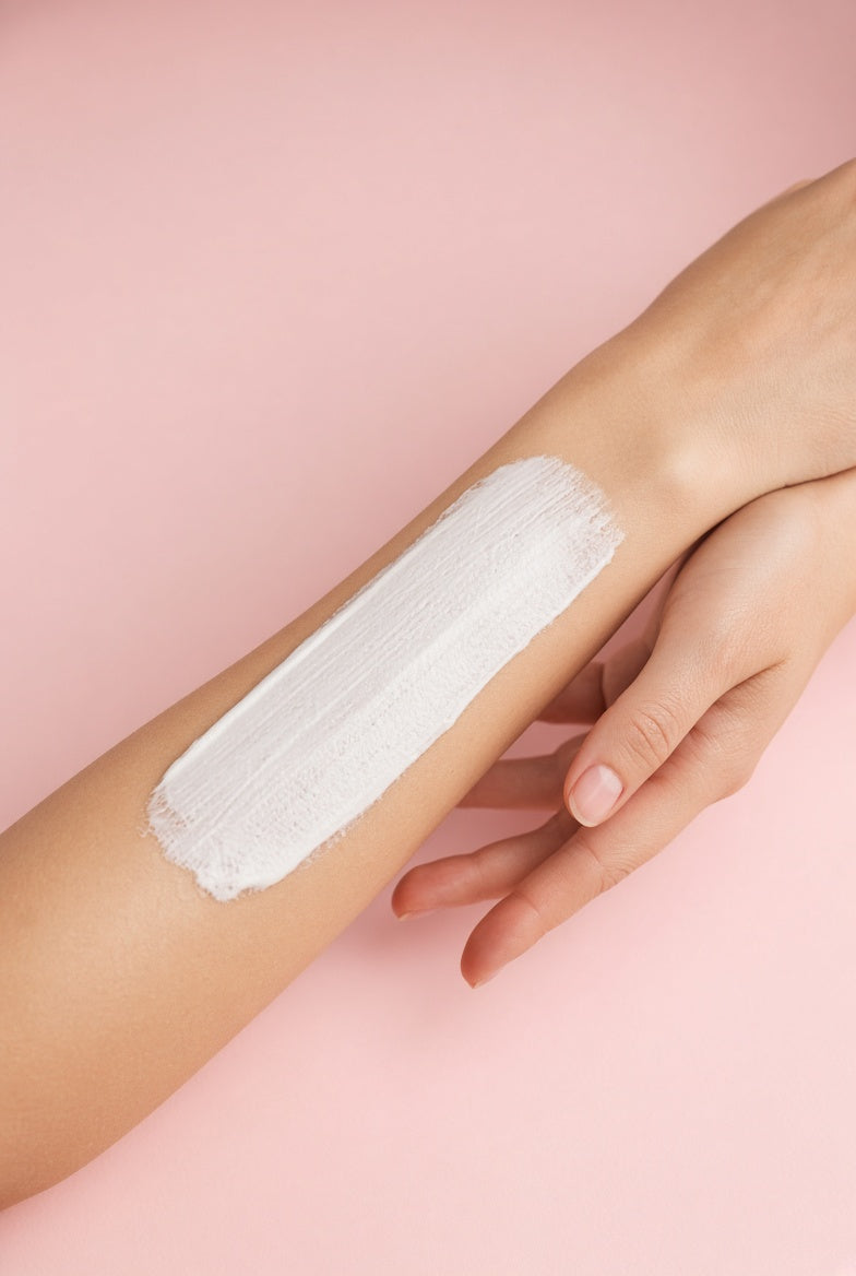 De la crème étalée sur un bras, sur fond rose